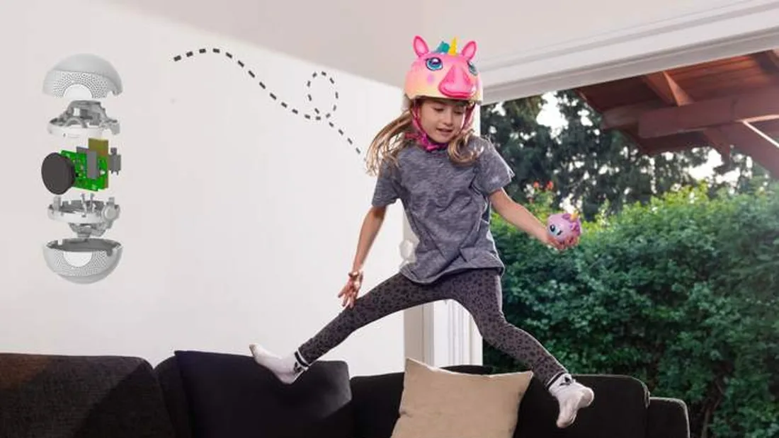 A girl in a unicorn mask leaping across a sofa holding a Storyball, next to an exploded view of the ball's parts